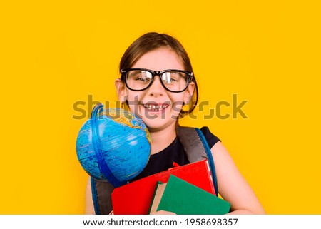 Girl kid 6 y.o. glasses with a books and globe looking at camera in isolation on a yellow background. Back to school.