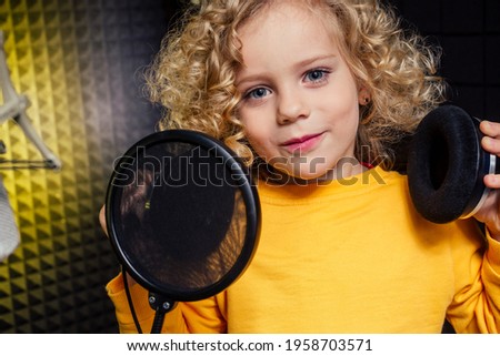 girl blonde curly hair style star singer artist in a yellow blouse with headphone recording new song with microphone.