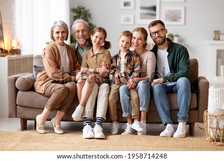 Big happy family. Portrait of grandparents, mother, father and two their cute kids, sister and brother, sitting together on coach at home and smiling at camera. Mortgage loan and real estate concept Royalty-Free Stock Photo #1958714248