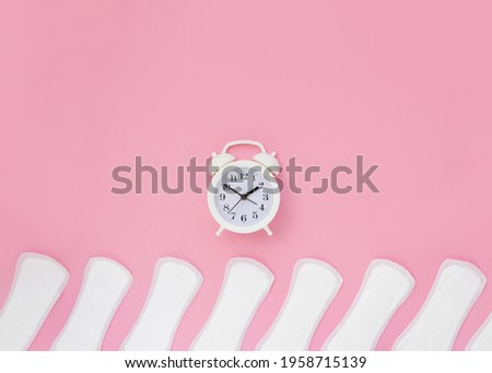 Female daily pads and alarm clock on pastel background. Concept of women's health and regular periods. Copy space