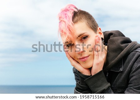 portrait of punk girl with pink hair looking at camera sweetly. Happy and serene woman with her hands on her face and with the sea in the background. urban tribes and youth Royalty-Free Stock Photo #1958715166