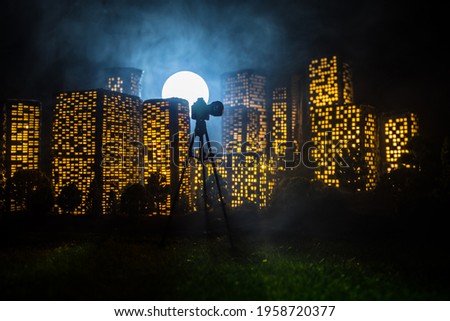 Cartoon style city buildings. Digital camera with tripod taking night shots of miniature city. Photographer with camera at night. Selective focus.