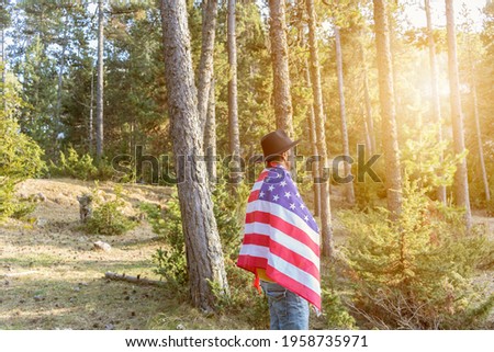 United States Independence day celebration concept, 4th of July.Man in black cowboy hat holding american flag at sunset in the forest park.