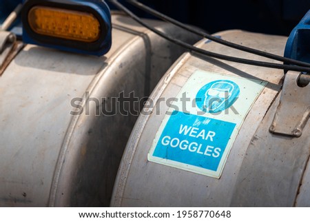 "Wear goggles" safety warning information on metal part of fuel tanker pumping unit, emphasize the worker need to wear safety equipment before working. Industrial safety sign object.
