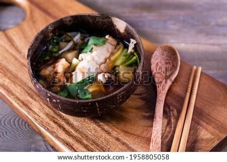 Asian soup with halibut and seafood (hemultan) shrimps, mussels and young octopus. Korean traditional soup on a dark wooden background with herbs. Wooden plate and spoon.