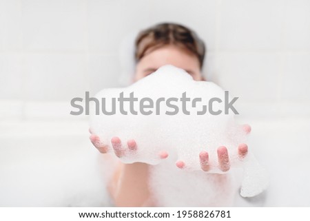 girl playing with bath foam in the bathroom. little girl making froth and holding it in hands. kids hygiene, evening routine. having fun in bathtube.