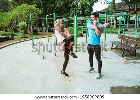 a young man and a girl in a veil chatting while standing doing warm-up movements before exercising in the park