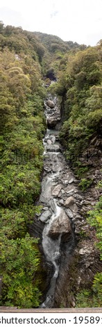 Vertical panoramic view of mountain stream flowing into glacial valley of Franz Josef Glacier National Park, New Zealand