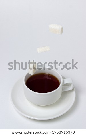 Sugar cubes fall into a cup of tea on a white background. A cup of tea with refined sugar. Tea time
