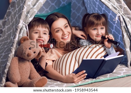 Woman and her little children reading book in play tent at night Royalty-Free Stock Photo #1958943544