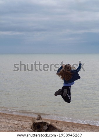 Rear view of a jumping girl on the beach. A happy teenage girl in clothes pretends to fly into the water. The concept of freedom, independence and a quick holiday break. Space for your text.