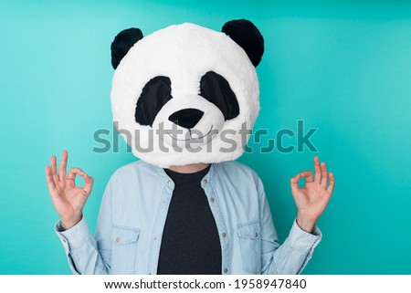 Young man wearing panda mask over isolated aquamarine studio background in zen pose
