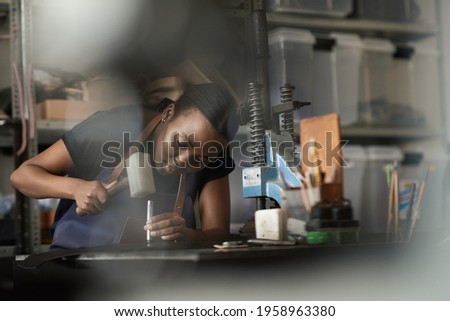 African female artisan working on leather with a mallet and punch Royalty-Free Stock Photo #1958963380