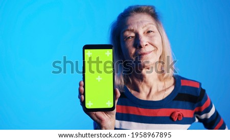 Old caucasian woman showing smartphone with green screen. High quality photo