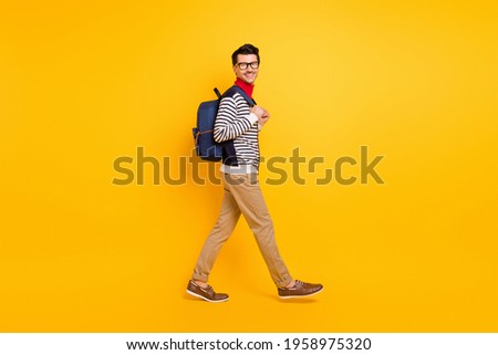 Full size profile photo of friendly young man walking carry bag look camera isolated on yellow color background