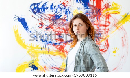 Hand painting. Street art. Creative graffiti design. Portrait of confident talented woman artist standing at blur colorful blue red yellow abstract pattern artwork on white wall poster background.
