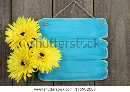 Blank antique teal blue sign with three bright sunflowers hanging on rustic wooden background