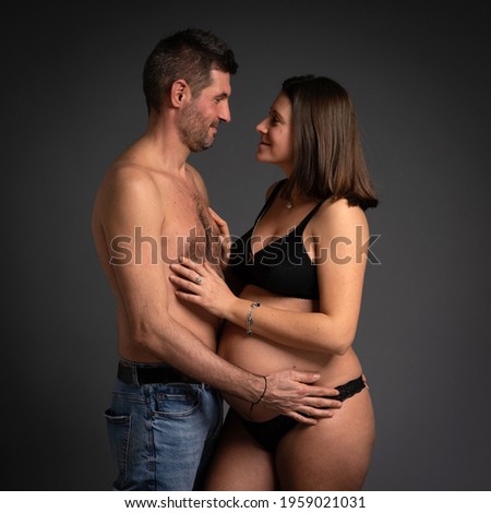 Couple studio intimate portrait. Man and pregnant woman hugging and looking at each others. 