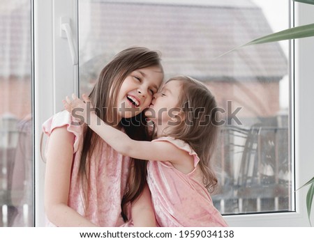 Two sisters hugging at home. Little girls with positive emotion wear pink casual dresses. Family relationships concept