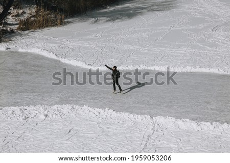 Stylish man in black clothes, a tourist with a backpack on his back jumps, dances and has fun on a snowy, icy road along the river in winter. Photography, copy space.