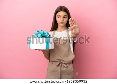 Little girl with a big cake over isolated pink background making stop gesture and disappointed