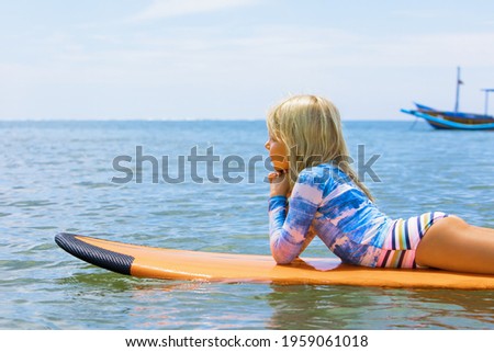 Happy girl relaxing before surfing. Surfer lying on surf board, look at sky. People in water sport adventure camp, extreme activity on family summer beach vacation. Watersport background