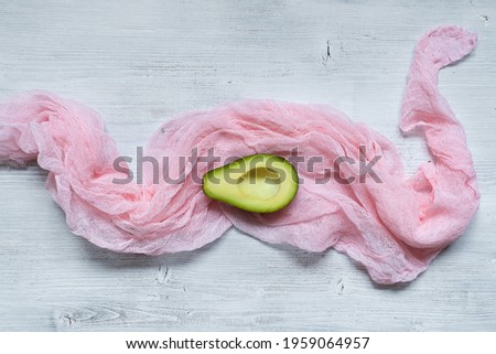 Green fresh avocado, cut in half, on a pink light fabric, lying on a wooden blue background. Minimalist photo in rustic style. Vitamin, vegan nutrition concept