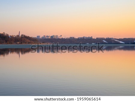 Cityscape at golden sunset with buildings reflecting in the lake. Early spring season and remainings of semi-melted ice.
