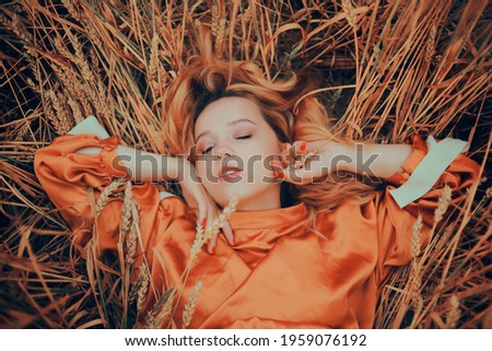A girl in a golden wheat field lies in a dress. A woman is sleeping in nature, the model has closed her eyes and enjoys fresh air