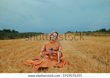 A beautiful girl in a dress sits on a wheat field. Fabulous photo of a blonde outside the city. A woman without allergies holds blue flowers.