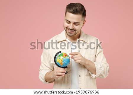 Young smiling geography student teacher happy man 20s in jacket white t-shirt holding in hands spin Earth world globe isolated on pastel pink color background studio portrait. Lifestyle people concept