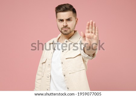 Young serious strict trendy caucasian man 20s wearing jacket white t-shirt do stop palm gesture refusing saying no isolated on pastel pink color background studio portrait. People lifestyle concept