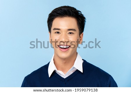 Close up portrait of young handsome smiling Asian man face on light blue studio background Royalty-Free Stock Photo #1959079138