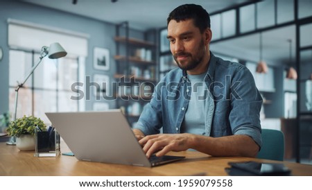 Handsome Caucasian Man Working on Laptop Computer while Sitting on a Sofa Couch in Stylish Cozy Living Room. Freelancer Working From Home. Browsing Internet, Using Social Networks, Having Fun. Royalty-Free Stock Photo #1959079558