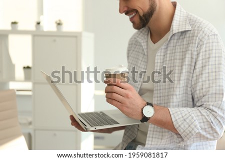 Freelancer with cup of coffee working on laptop indoors, closeup