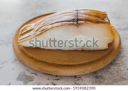 Smoked halibut on a round wooden board against the background of a gray tabletop. Smoked turbot.