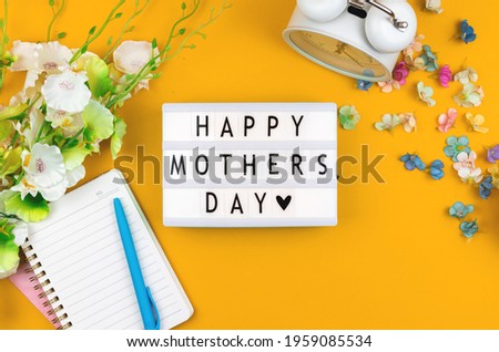 Happy Mothers Day text message on lightbox, greeting card flat lay concept with yellow background and spring flowers, top view