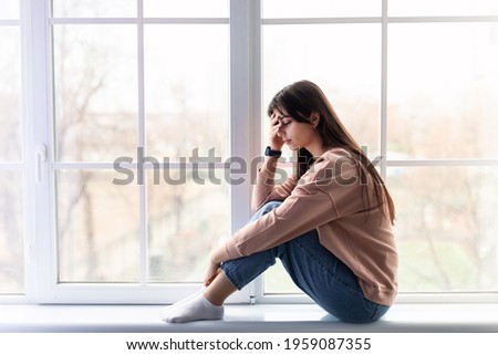 Profile side view of sad young woman sitting on windowsill, covering face. Frustrated exhausted female feeling unhappy about problems, break up with boyfriend or unexpected pregnancy concept Royalty-Free Stock Photo #1959087355