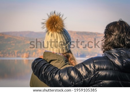 Young couple looks into the distance to the opposite shore of the lake in the autumn forest