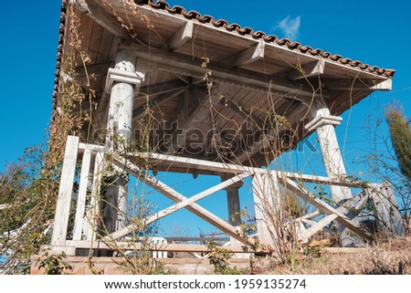 White wooden gazebo in the garden overgrown with plants on the blue sky background