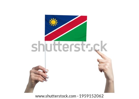 A beautiful female hand holds a Namibia flag to which she shows the finger of her other hand, isolated on white background.