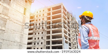 Rare view of a Young Asian male Engineer or Architect wearing Protective gears and looking at the Constructing building ongoing in the construction site. Proud face. Civil. Businessman.  Royalty-Free Stock Photo #1959163024