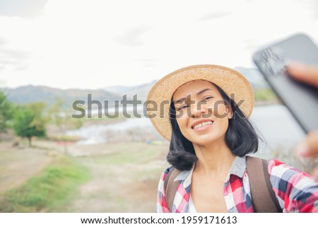 woman stand on the banks of the lake using mobile phone takes a picture selfie, taking pictures, Video call, Asian woman hiker in front smiling happy, Woman hiking in woods, warm summer day.