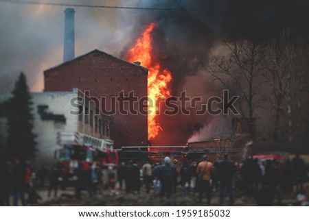 Massive large blaze fire in the city, brick factory building on fire, hell major fire explosion flame blast,  with firefighters team firemen on duty, arson, burning house damage destruction  Royalty-Free Stock Photo #1959185032