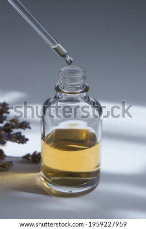 Drop on a pipette over glass dropper bottle with skin care cosmetic. Butter, serum, or tincture with hard shadow
