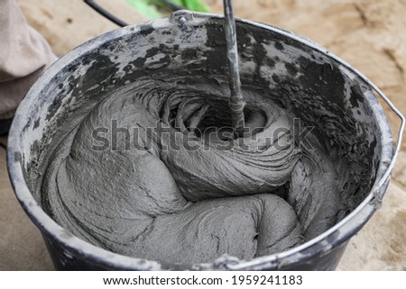Cement based adhesive. Mixing concrete with an electric drill and mixer. Wet mortar for finishing works in construction. Close-up. Selective focus. Royalty-Free Stock Photo #1959241183