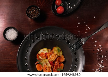 Delicious shrimp salad with vegetables in a black plate on a dark wooden background. Beautiful decoration and serving of the dish. Healthy and dietary food. Photo flat lay.