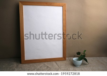 White paper in a wooden frame on a table covered with linen canvas. Mockup.
