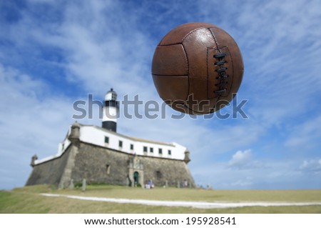 Vintage brown football flying mid-air in blue sky above the famous Farol da Barra lighthouse in Salvador