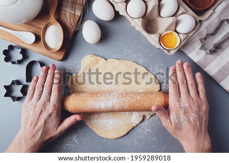 The girl rolls out the dough with a wooden rolling pin for making cupcakes or cookies. Flat composition with kitchen utensils and ingredients, copy space. Concept of baking for the holiday.
